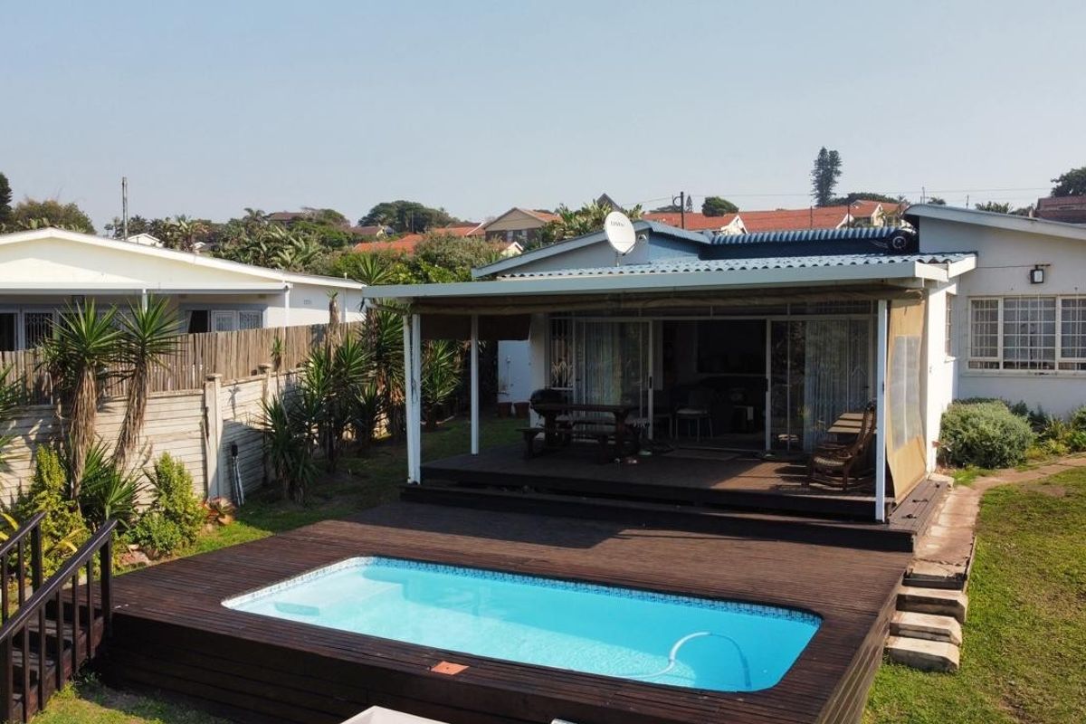 Rear view of the property featuring a swimming pool, timber decking, and a covered patio area with sliding glass doors.