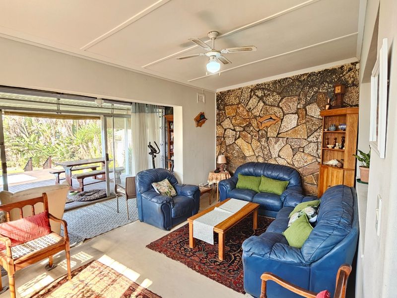 Spacious living room featuring a distinctive stone accent wall, ceiling fan, and large sliding glass doors providing seamless access to the outdoor patio area.