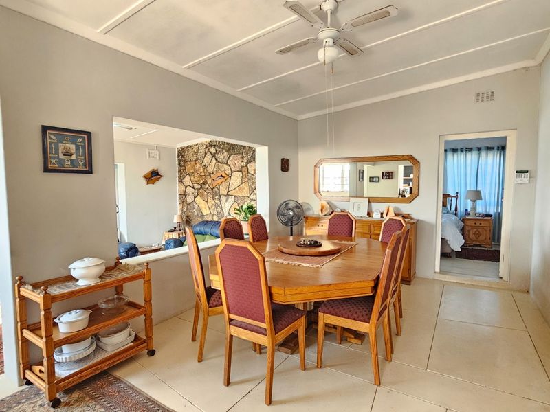 Spacious dining room featuring tiled flooring, a ceiling fan, and an open-plan layout connecting to an adjacent living area with a stone feature wall.