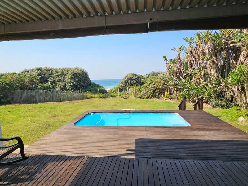 Outdoor entertainment area featuring a swimming pool set within timber decking, overlooking a garden with ocean views.