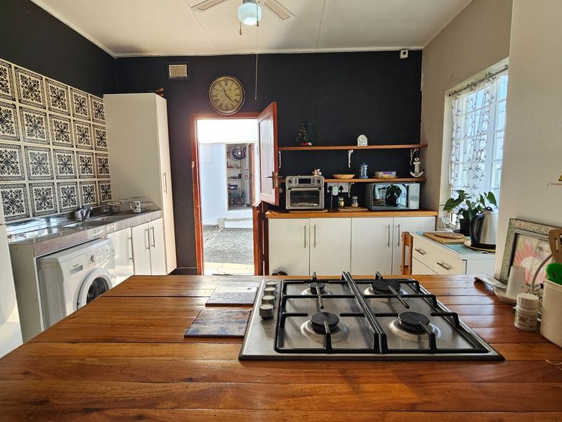 A functional kitchen featuring a wooden island with a built-in gas hob, white cabinetry, patterned tile backsplash, and direct access to an outdoor area.