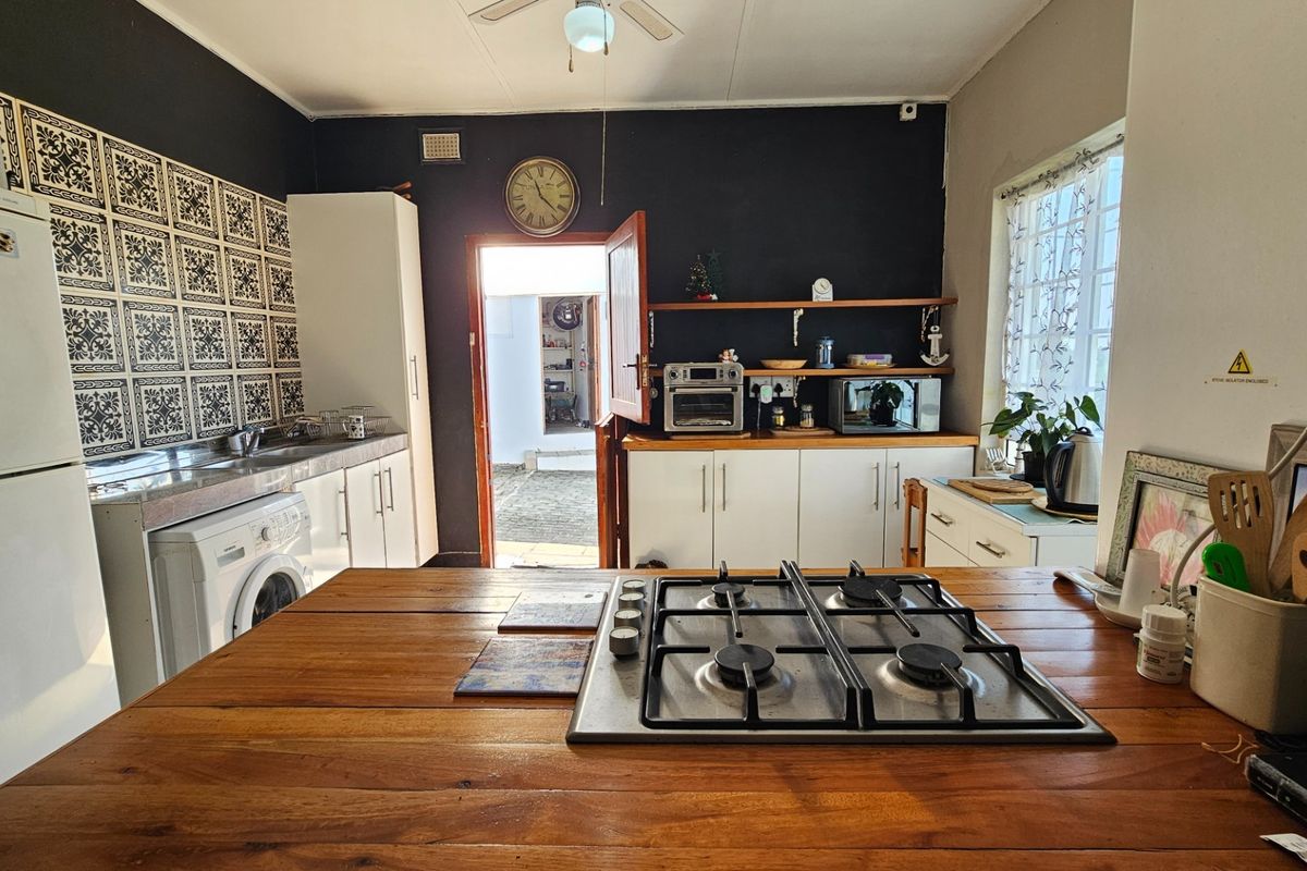 A functional kitchen featuring a wooden island with a built-in gas hob, white cabinetry, patterned tile backsplash, and direct access to an outdoor area.