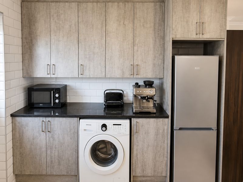 A functional laundry area featuring modern grey wood-look cabinetry, black stone countertops, and a white subway tile backsplash.