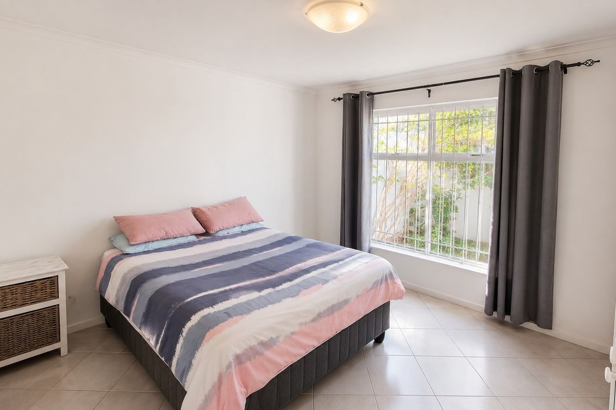 A bright and well-maintained bedroom featuring neutral tiled flooring, coved cornicing, and a large window fitted with security bars.