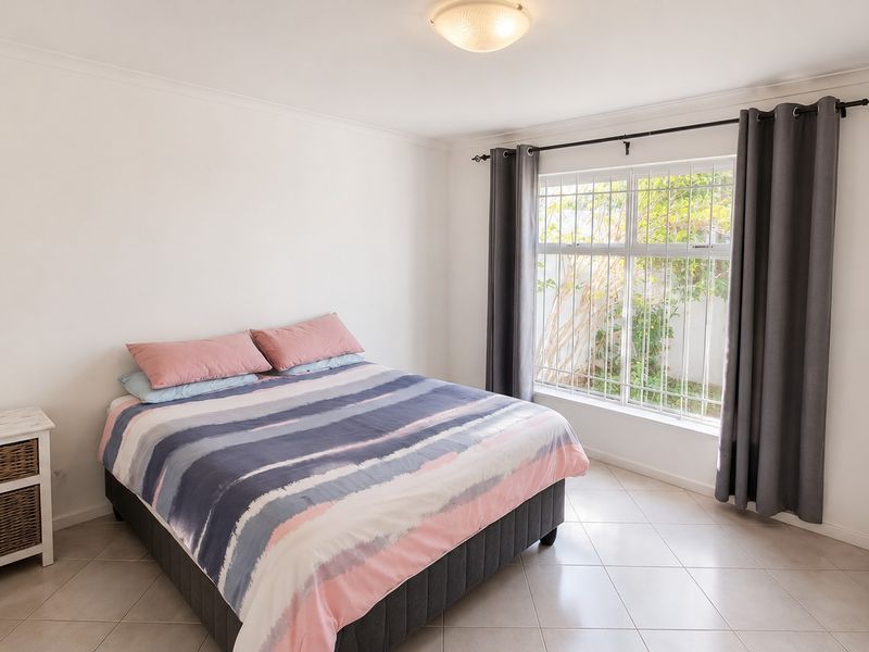 A bright and well-maintained bedroom featuring neutral tiled flooring, coved cornicing, and a large window fitted with security bars.