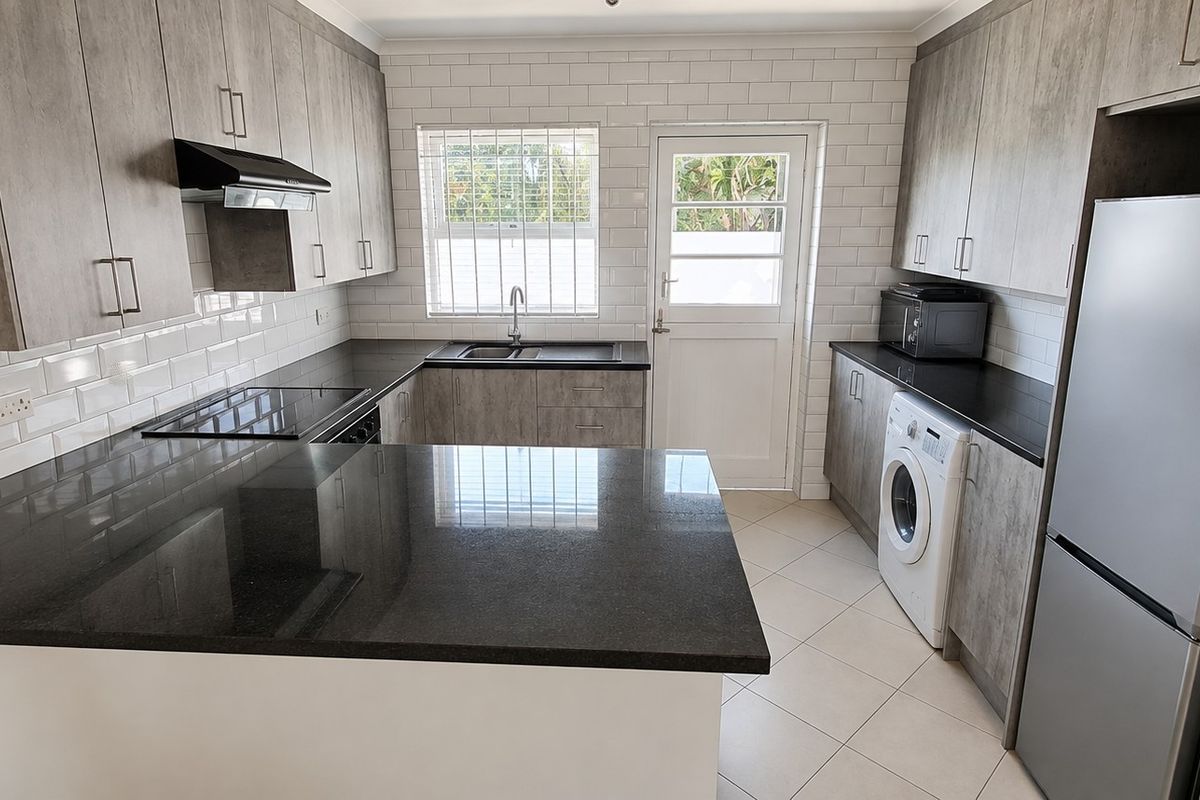 Modern kitchen featuring granite countertops, subway tile backsplash, built-in appliances, and ample cabinetry with direct access to the exterior.