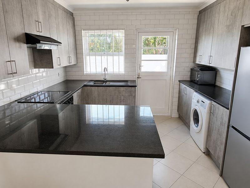 Modern kitchen featuring granite countertops, subway tile backsplash, built-in appliances, and ample cabinetry with direct access to the exterior.