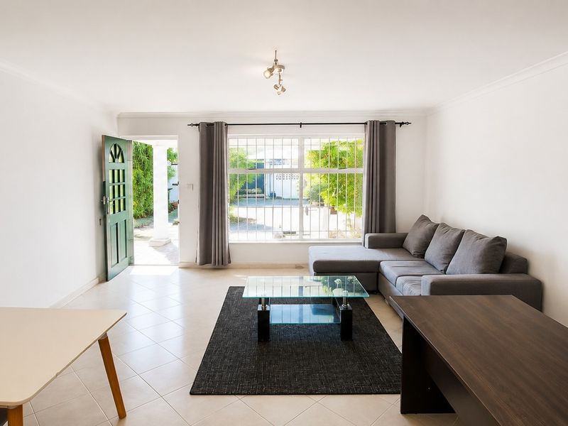 A bright, open-plan living area featuring tiled flooring, large windows for natural light, and direct access to the exterior entrance.