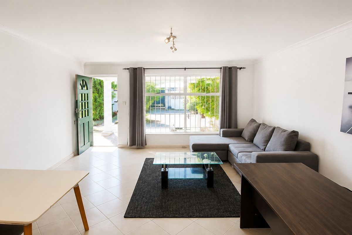 A bright, open-plan living area featuring tiled flooring, large windows for natural light, and direct access to the exterior entrance.