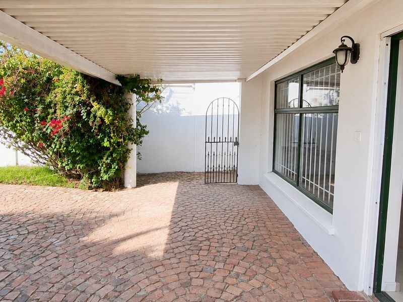 A covered patio area featuring cobblestone paving, a wrought iron gate, and direct access to the interior through a large window and door.