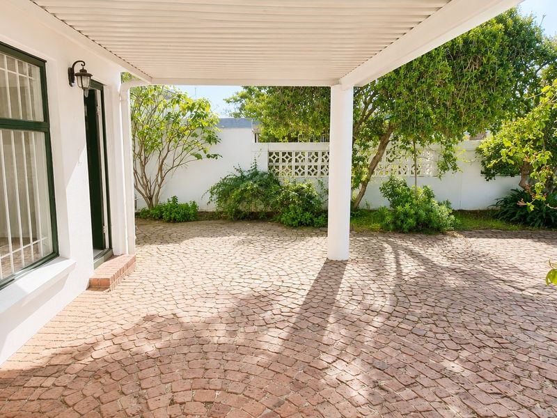 A covered outdoor patio area featuring cobblestone paving, a decorative boundary wall, and direct access to the garden.