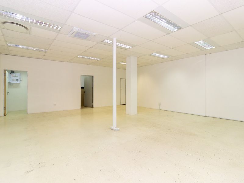 An empty open-plan retail space featuring a suspended ceiling with recessed lighting, a structural support column, and durable epoxy flooring.