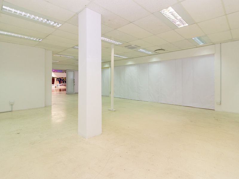 A spacious, empty retail unit featuring a suspended ceiling, recessed lighting, and a neutral open-plan layout suitable for various commercial uses.