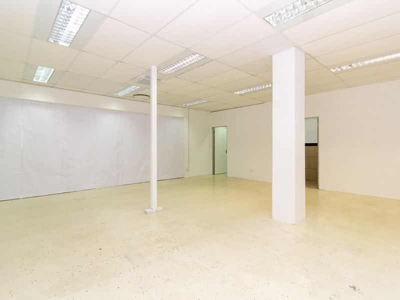 An open-plan retail space featuring a suspended ceiling with recessed lighting, a structural support column, and durable epoxy flooring.