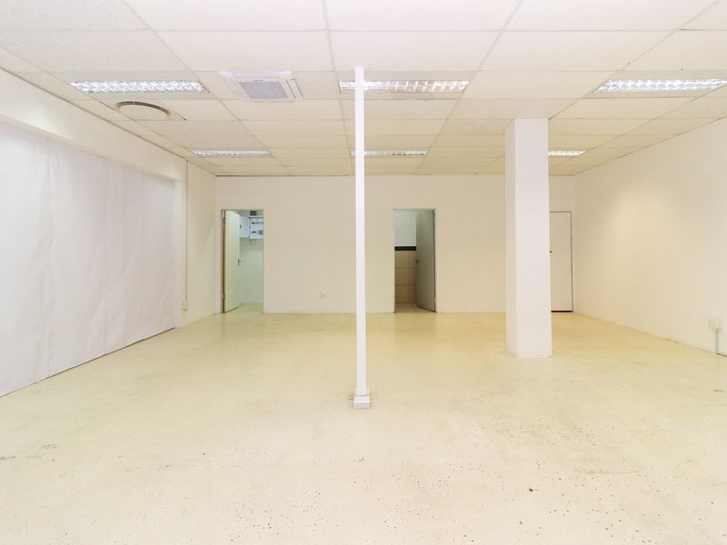A vacant open-plan retail space featuring a suspended ceiling, recessed lighting, and a durable epoxy floor finish, suitable for various commercial uses.