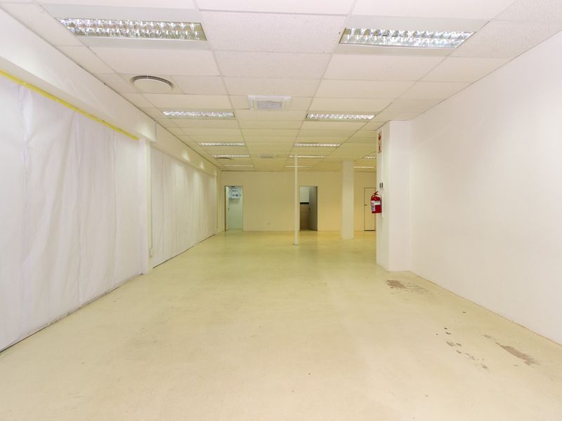 An open-plan retail space featuring a suspended ceiling with recessed lighting, concrete flooring, and a wall-mounted fire extinguisher.