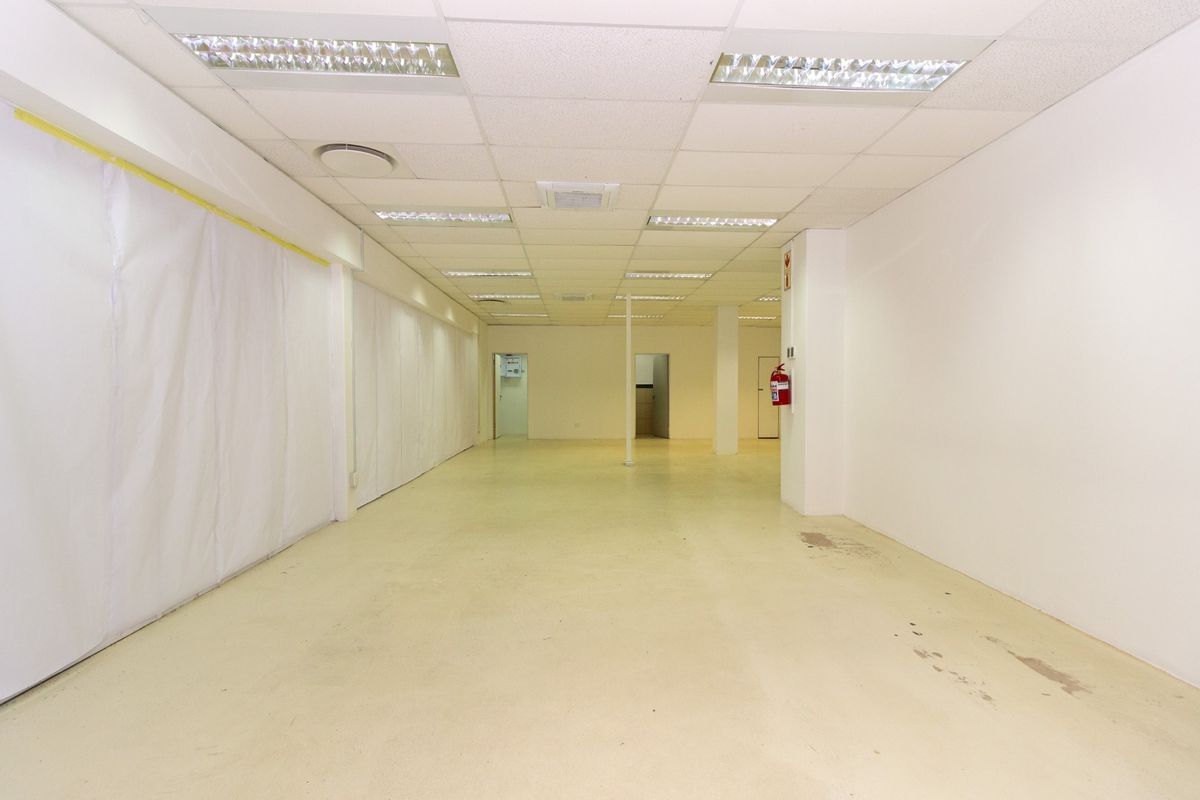 An open-plan retail space featuring a suspended ceiling with recessed lighting, concrete flooring, and a wall-mounted fire extinguisher.