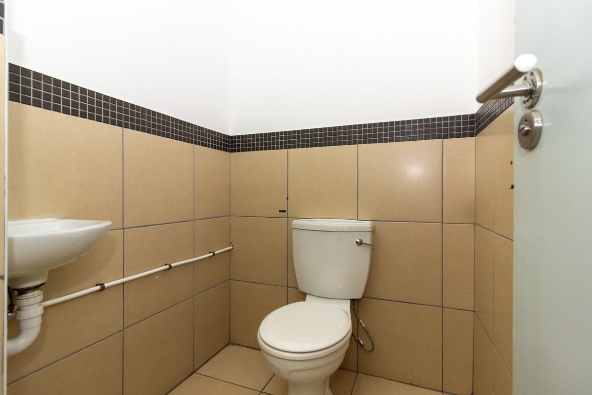 A functional bathroom featuring a standard toilet and wall-mounted basin with tiled walls and flooring.