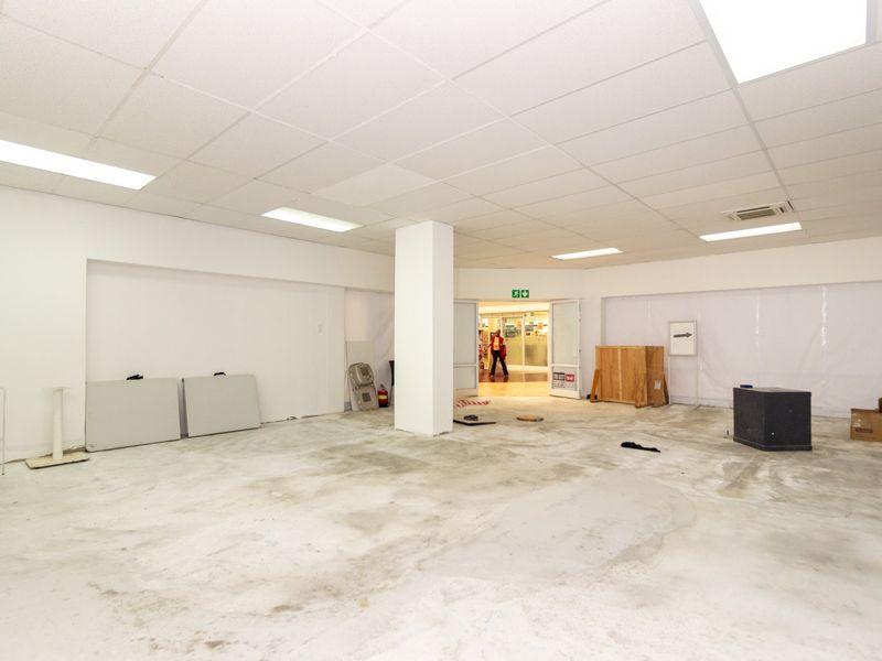 An open-plan retail space featuring a suspended ceiling with recessed lighting and a central support column, currently awaiting floor finishing.
