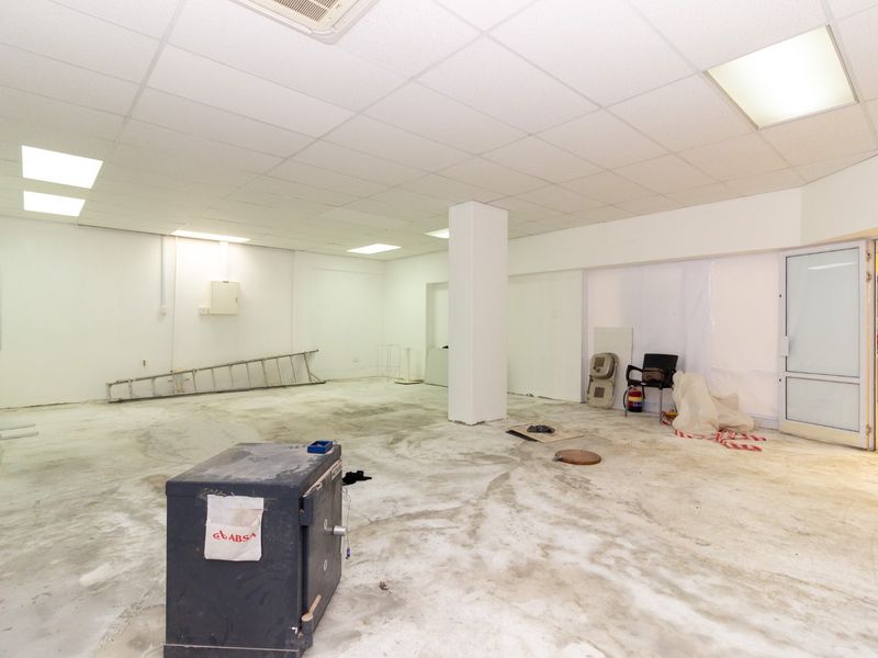 An open-plan retail space featuring a suspended ceiling, recessed lighting, and a concrete floor, currently in a shell condition ready for fit-out.