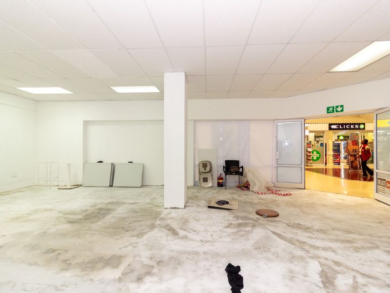 An open-plan retail space featuring a suspended ceiling, recessed lighting, and a structural column, currently awaiting flooring installation and final fit-out.