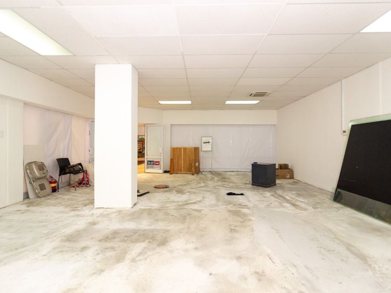 An open-plan retail space featuring a suspended ceiling, recessed lighting, a central structural column, and unfinished concrete flooring.