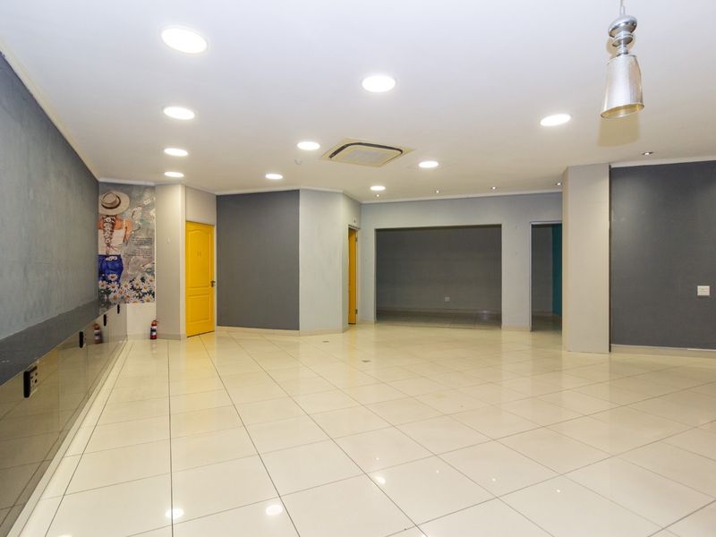 A spacious, open-plan retail area featuring polished tiled flooring, recessed downlighting, integrated air conditioning, and neutral grey wall finishes.