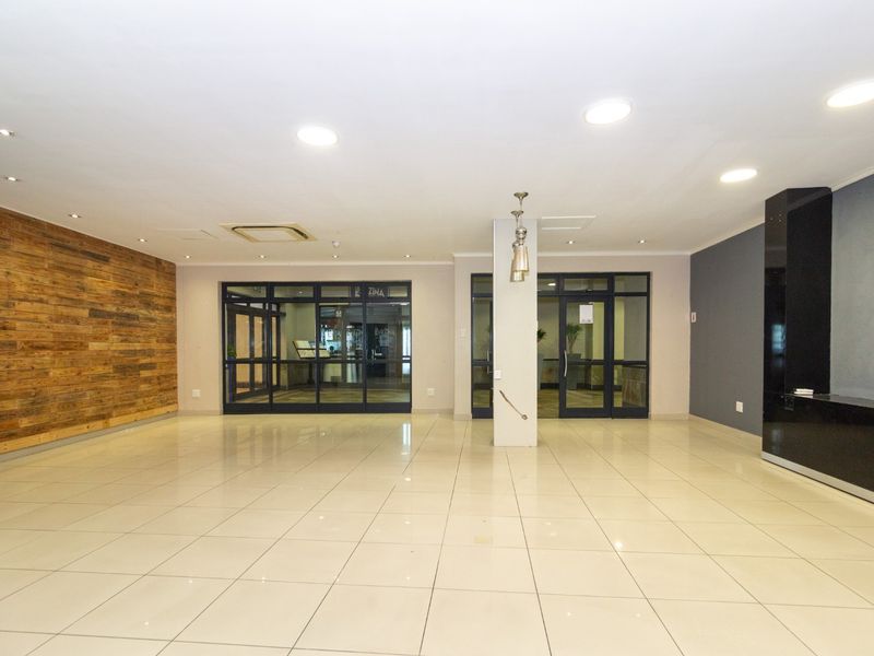 Spacious open-plan retail area featuring polished tile flooring, a decorative timber feature wall, and modern glass entrance doors with recessed lighting.