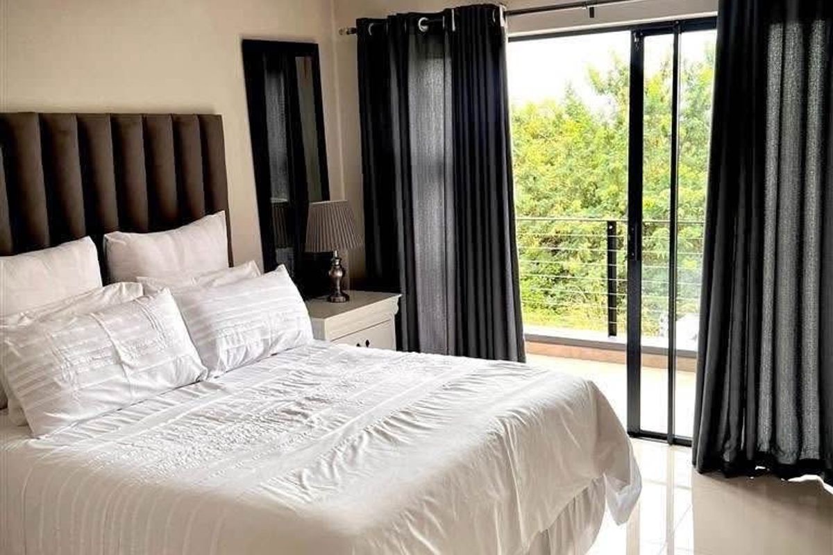 A well-maintained bedroom featuring tiled flooring, a wall-mounted air conditioning unit, and direct access to a private balcony through sliding glass doors.