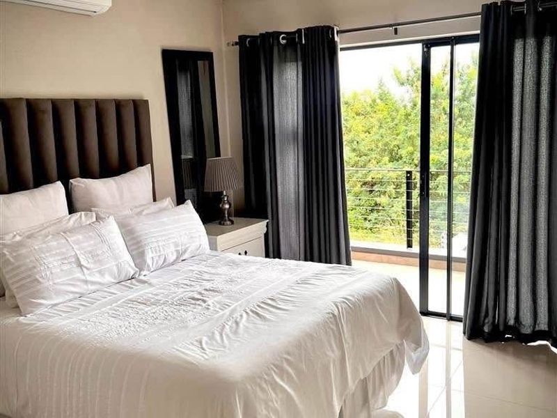 A well-maintained bedroom featuring tiled flooring, a wall-mounted air conditioning unit, and direct access to a private balcony through sliding glass doors.