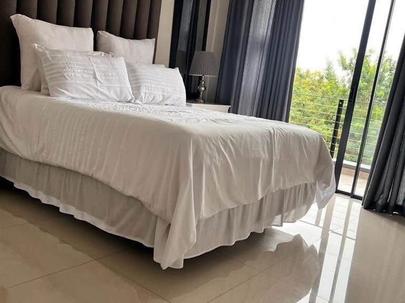 A well-maintained bedroom featuring polished tiled flooring, a split-system air conditioner, and direct access to a balcony through sliding glass doors.