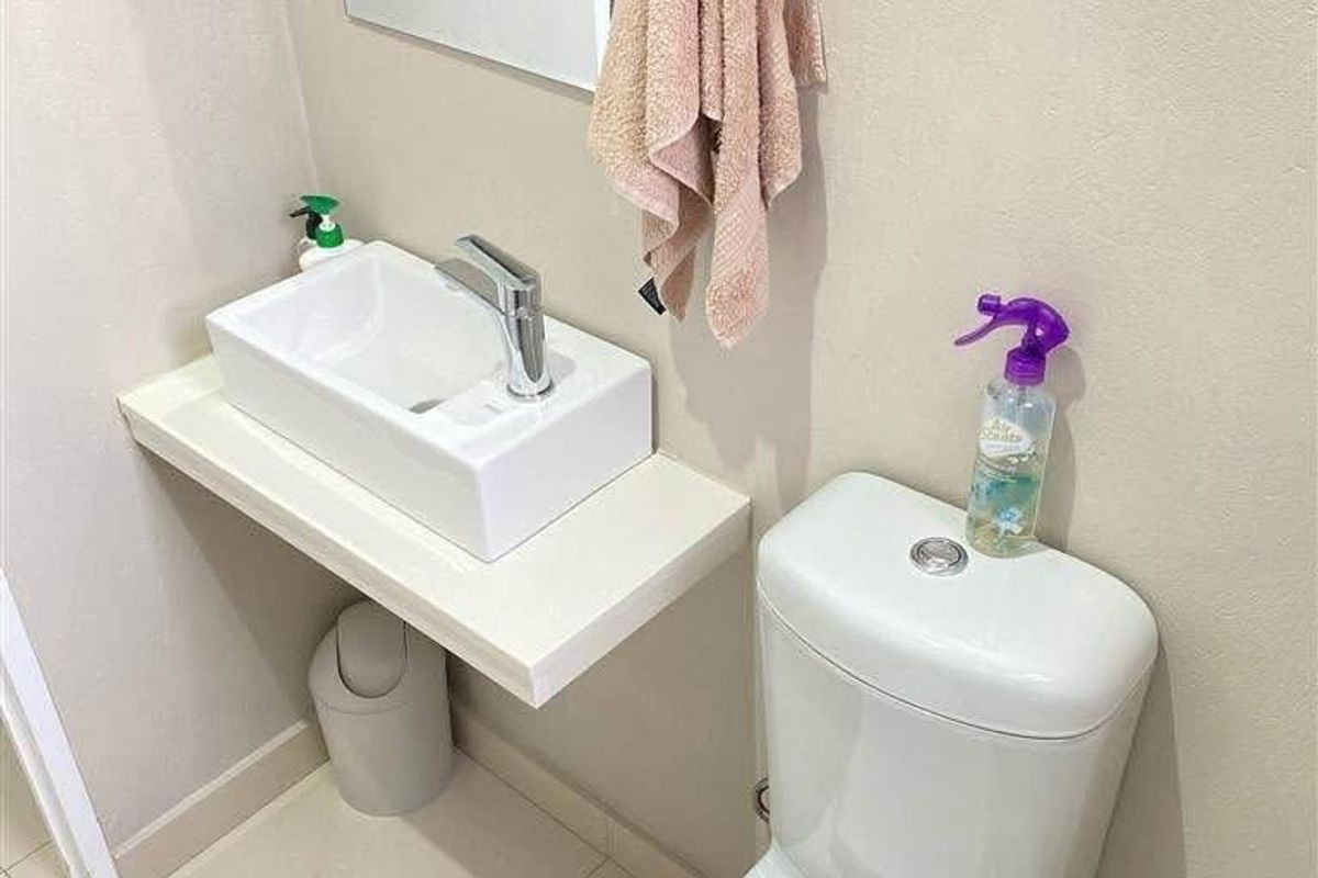 A compact, modern guest bathroom featuring a floating vanity shelf, vessel sink, and a dual-flush toilet with neutral floor tiling.