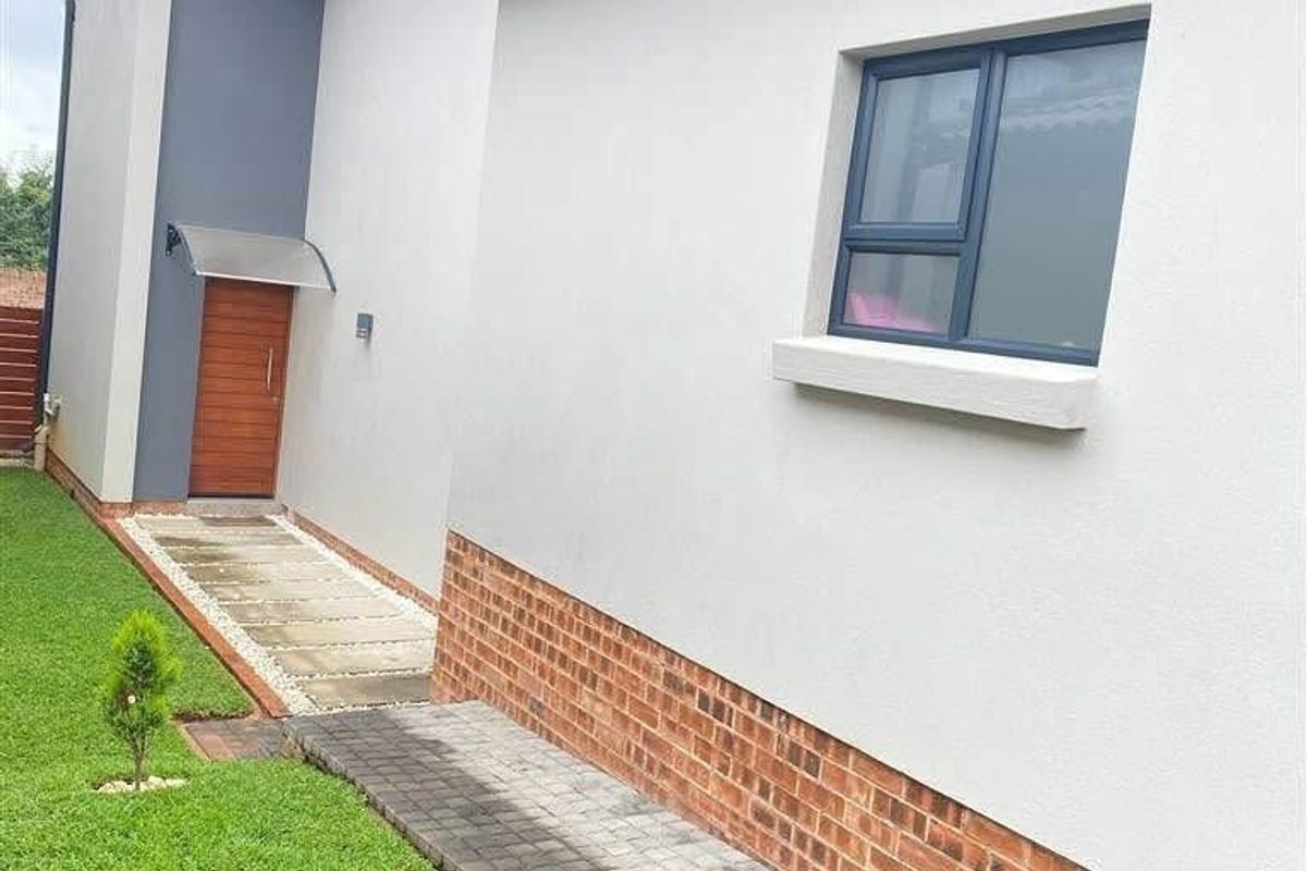 A well-maintained rear exterior view of the townhouse featuring a paved walkway, brick base detailing, and modern aluminium window frames.