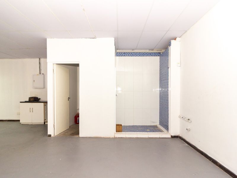An open utility space featuring a tiled shower enclosure, built-in cabinetry, and an electrical distribution board, suitable for various commercial or storage purposes.