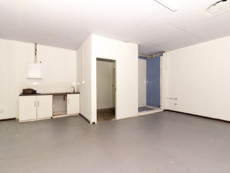 An empty utility space featuring a kitchenette area with sink, a tiled shower enclosure, and an electrical distribution board.