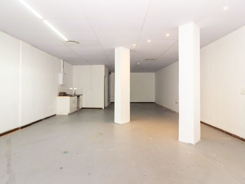 An open-plan retail space featuring a kitchenette, structural columns, and a suspended ceiling, offering a versatile layout for various business needs.