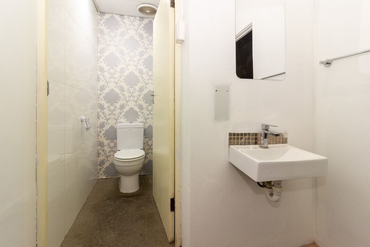 A compact bathroom featuring a wall-mounted basin, toilet, and extractor fan, requiring cosmetic updates to improve the overall finish.