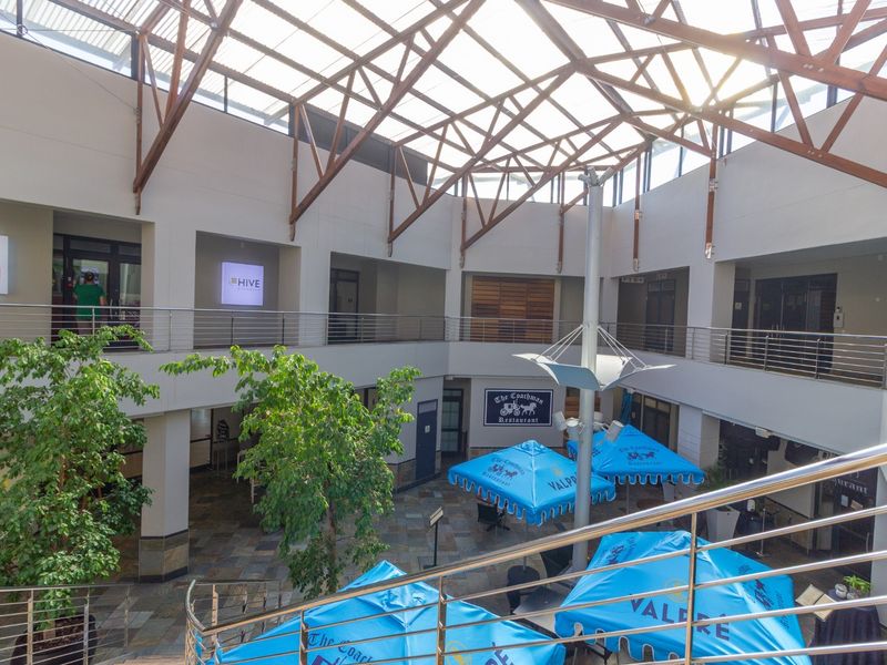 Spacious multi-level retail atrium featuring a high timber truss roof with skylights, stone flooring, and stainless steel balustrades overlooking a central courtyard area.