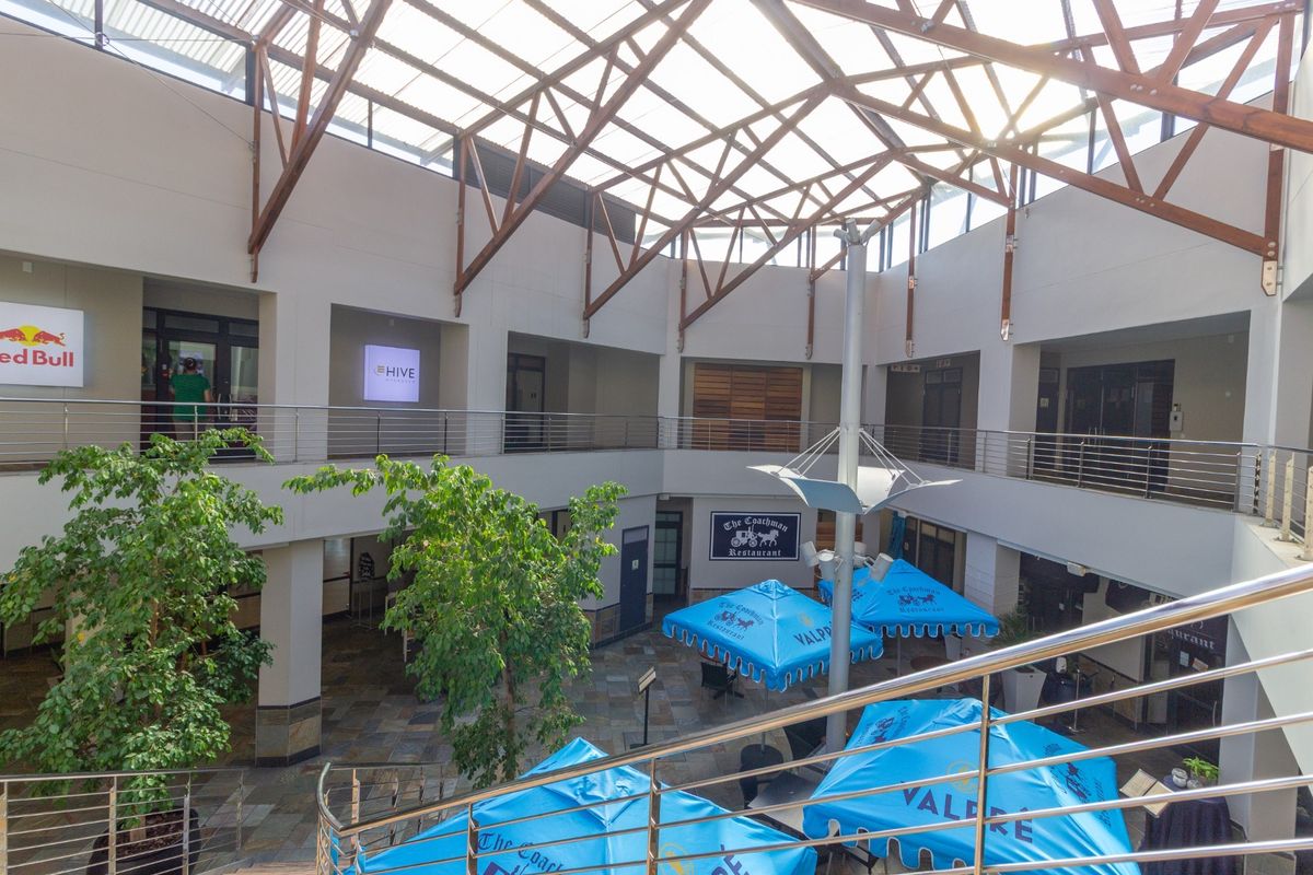 Spacious multi-level retail atrium featuring a high timber truss roof with skylights, stone flooring, and stainless steel balustrades overlooking a central courtyard area.
