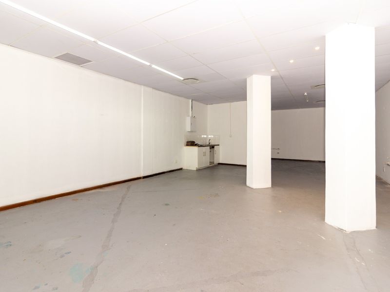 Open plan retail space featuring a suspended ceiling, structural columns, and a small kitchenette area with a sink.