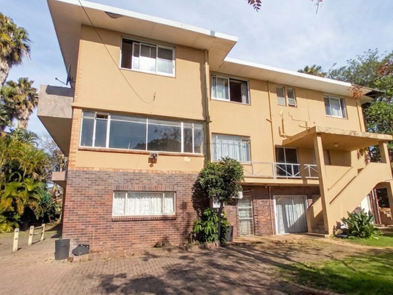 Rear view of a multi-story residential building featuring a combination of brick and stucco finishes, an external staircase, and a paved ground area.