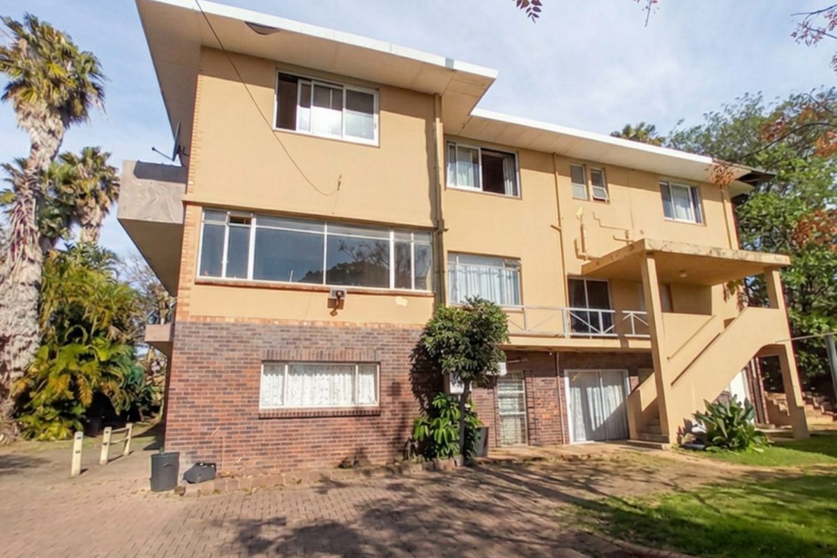 Rear view of a multi-story residential building featuring a combination of brick and stucco finishes, an external staircase, and a paved ground area.