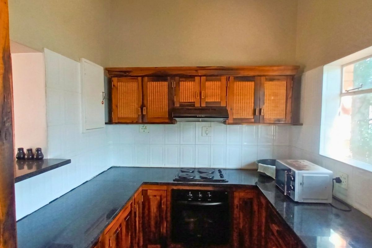 A functional kitchen featuring wooden cabinetry, black granite countertops, a built-in oven, electric hob, and a tiled backsplash.