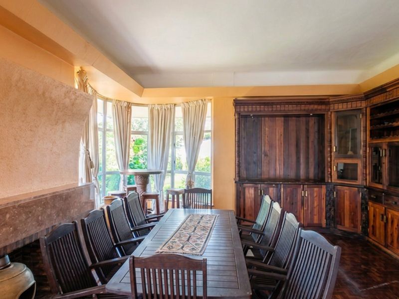 Spacious dining room featuring rich parquet flooring, a built-in wooden cabinetry unit, and a fireplace, complemented by a large bay window.