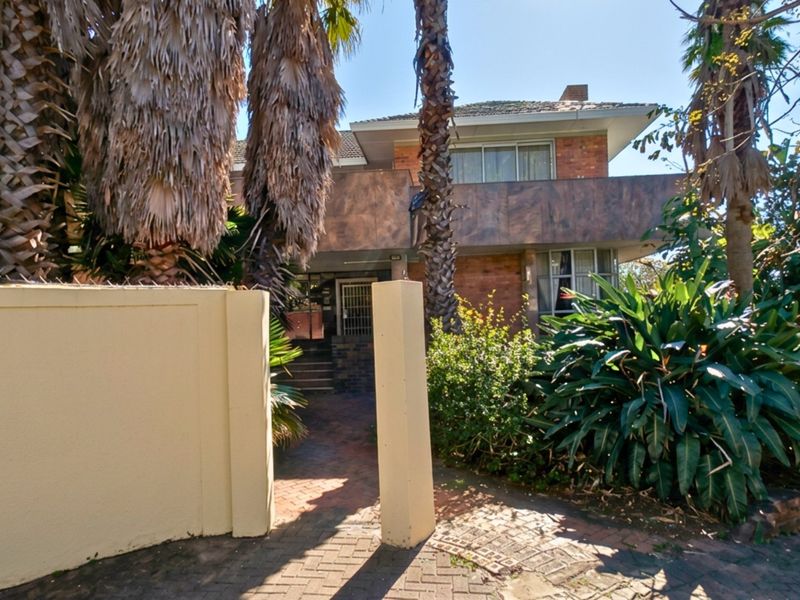 Front exterior view of a multi-story brick house featuring a paved entrance, perimeter wall, and mature landscaping.