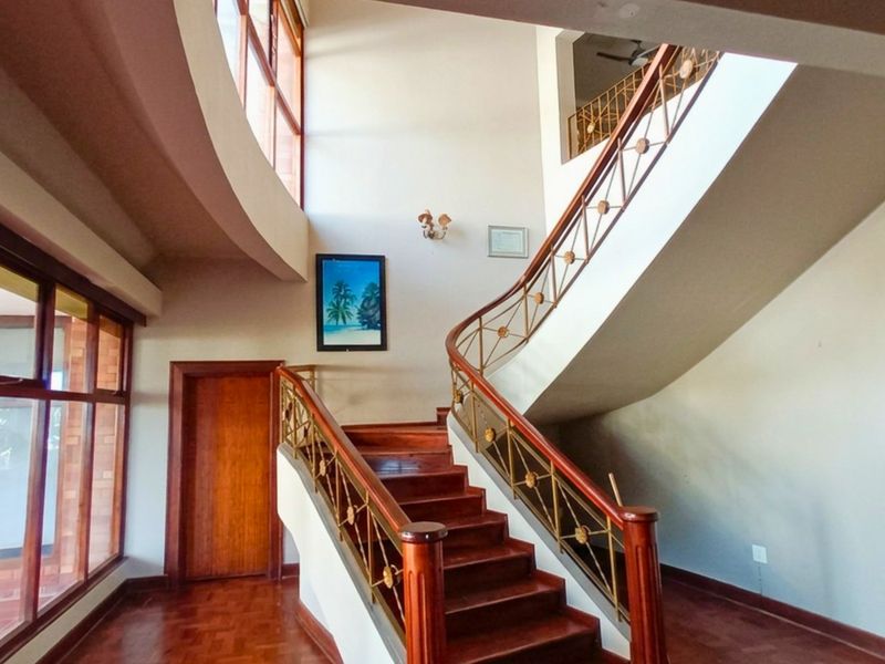 Spacious double-volume entrance hall featuring a grand curved staircase with wooden treads and decorative metal balustrades, complemented by large windows and wooden flooring.