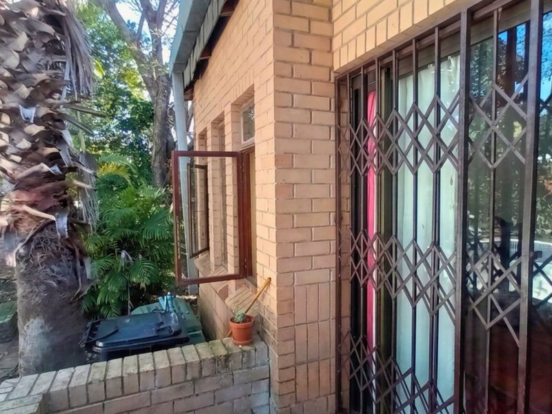 Rear exterior view of the property featuring brick facade, security gate, and sliding door access to the garden area.