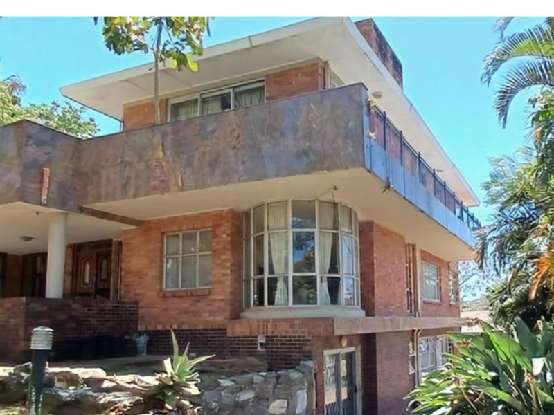 A multi-level brick house featuring a prominent balcony, bay window, and established garden surroundings, showcasing a classic architectural style.