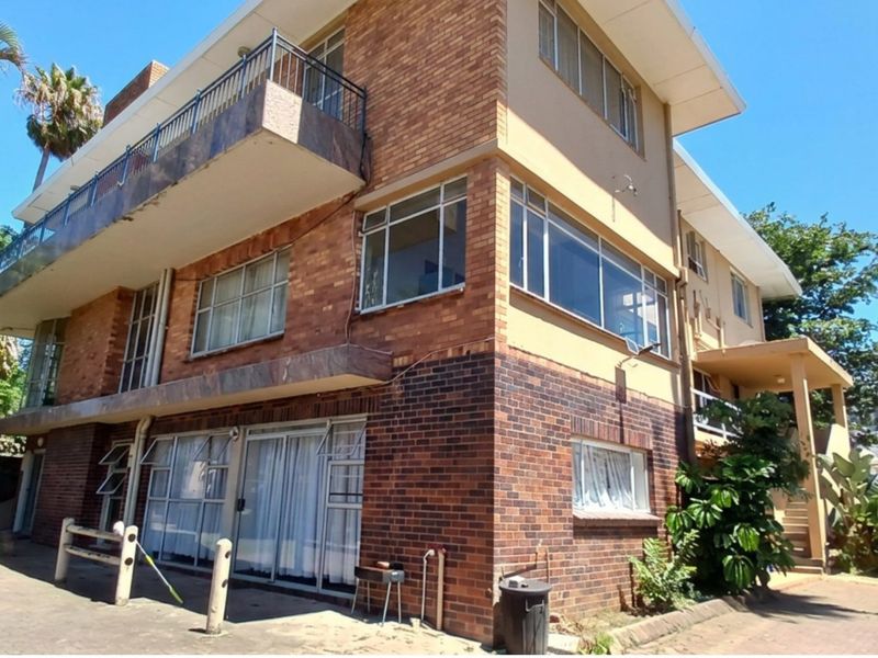 A multi-story residential building featuring a classic brick facade, upper-level balcony with metal railings, and large windows providing ample natural light.