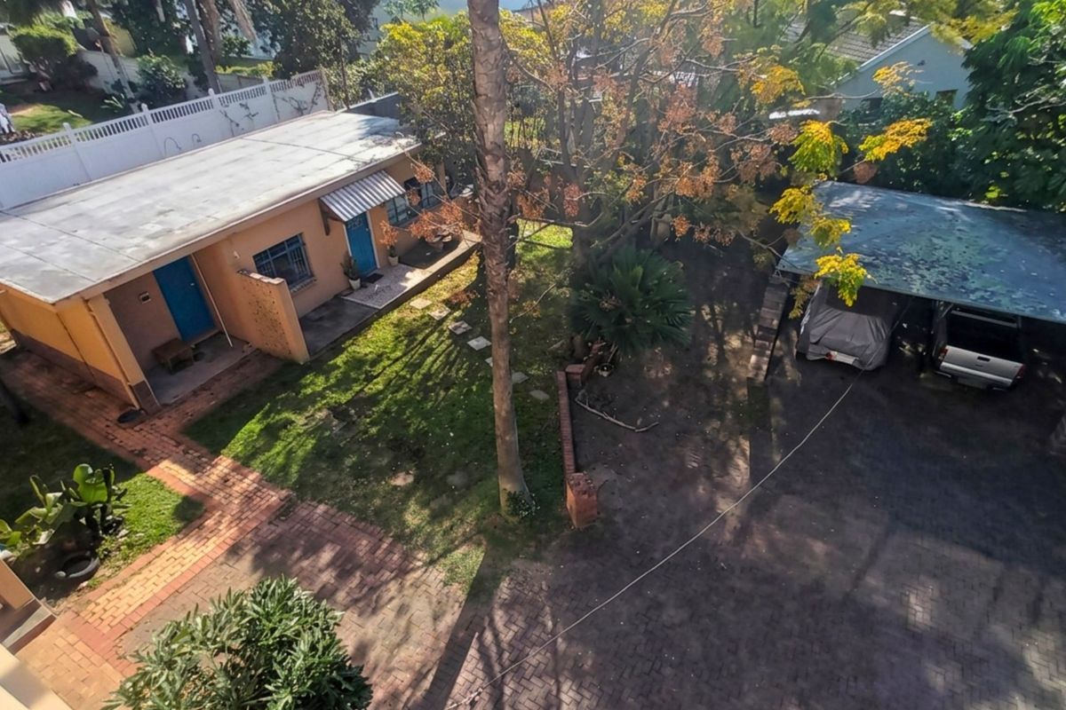 Aerial view of the property grounds featuring a paved driveway, a covered carport, a brick walkway, and a flat-roofed residential building.